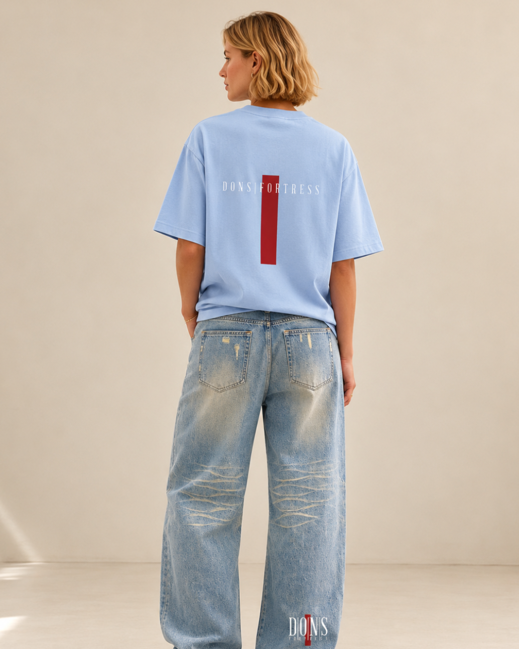 Person wearing a light blue t-shirt and jeans with visible branding, standing against a neutral background.