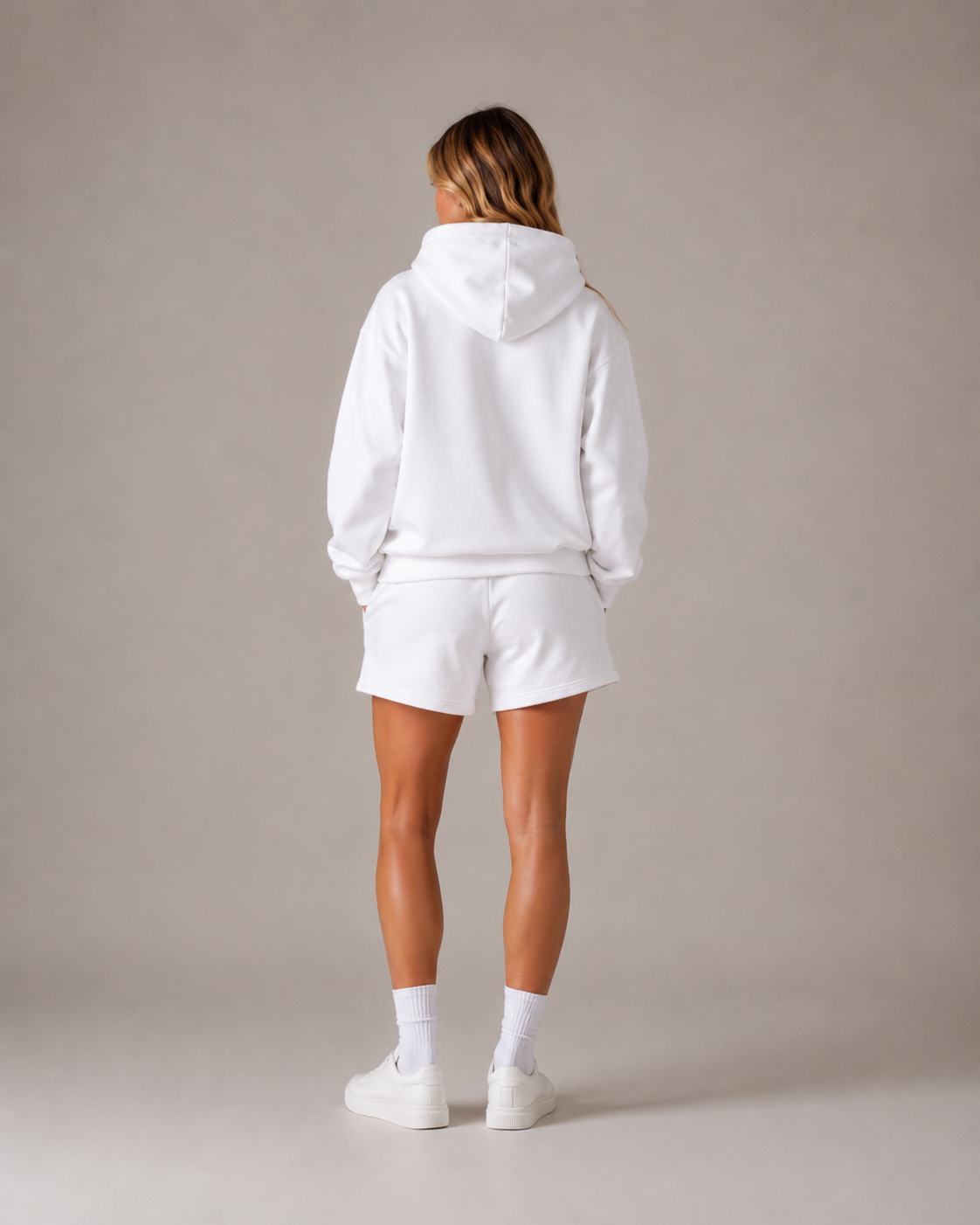 Person wearing a white hoodie and shorts set on a plain background