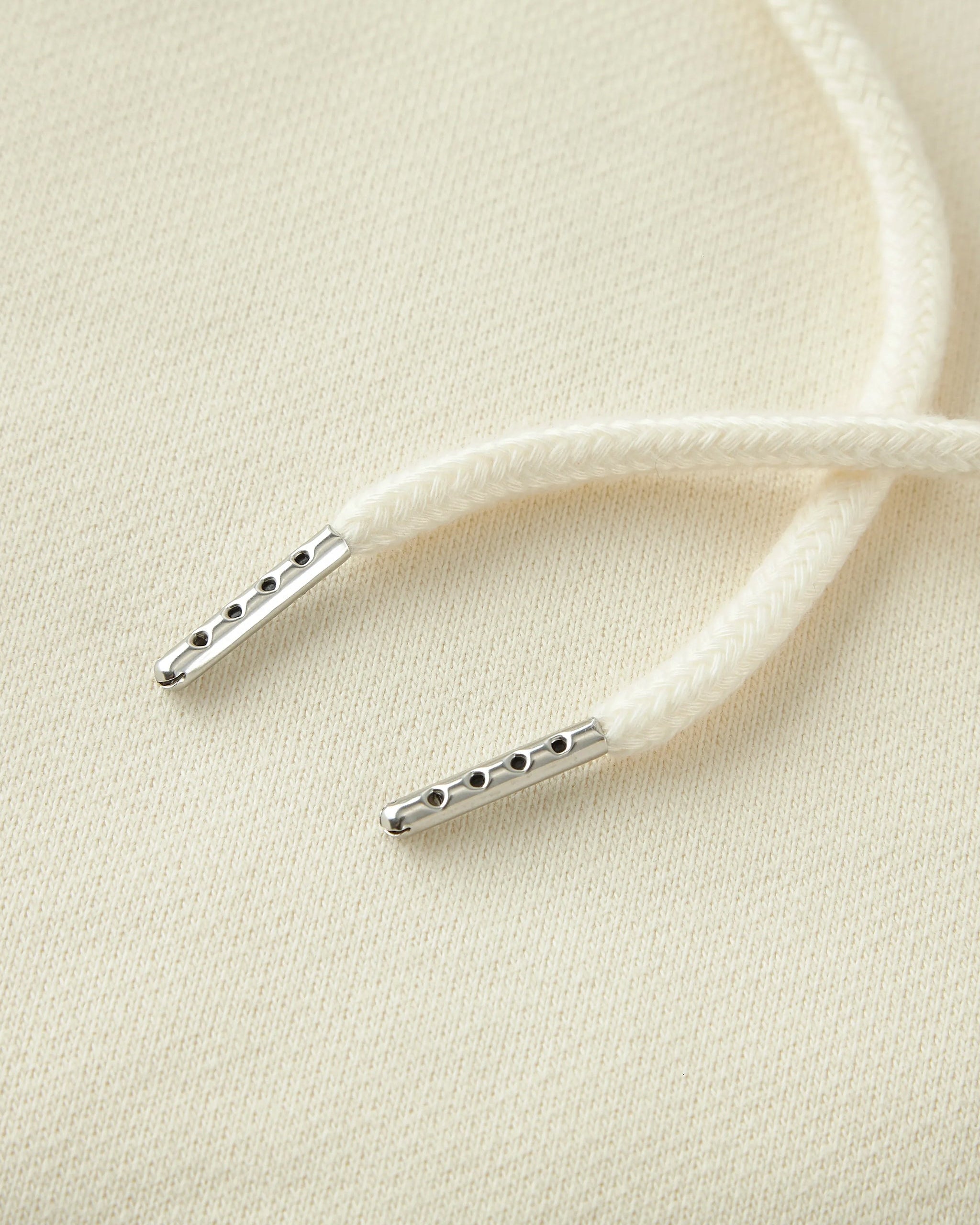 Close-up of white shoelaces with metal lace locks on a beige background