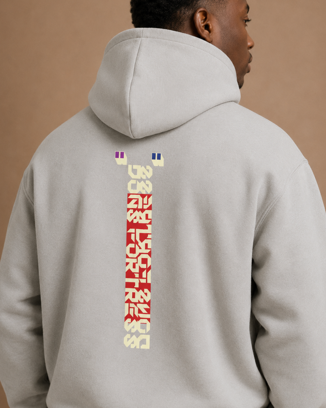 Person wearing a light gray hoodie with colorful text on the back against a beige background