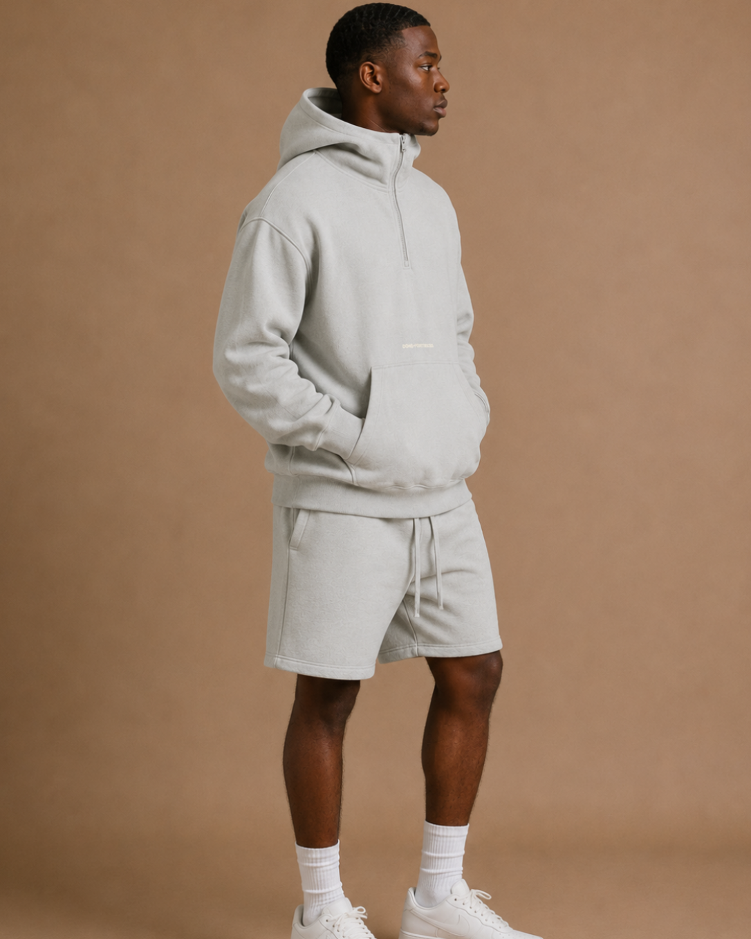 Man wearing a light gray hoodie and shorts set on a brown background