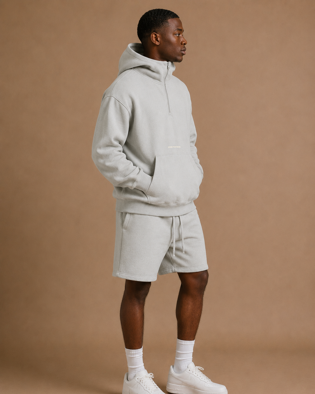 Man wearing a light gray hoodie and shorts set on a brown background