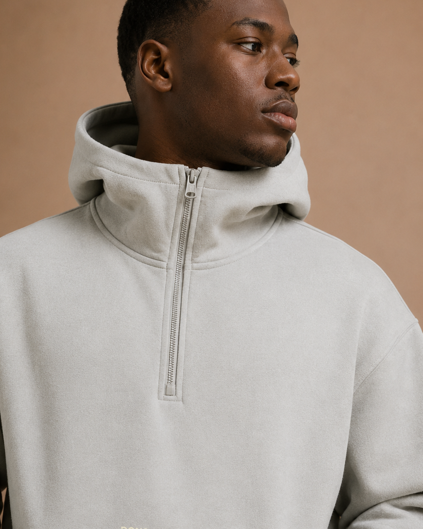 Man wearing a light gray hoodie with a brand logo on a beige background