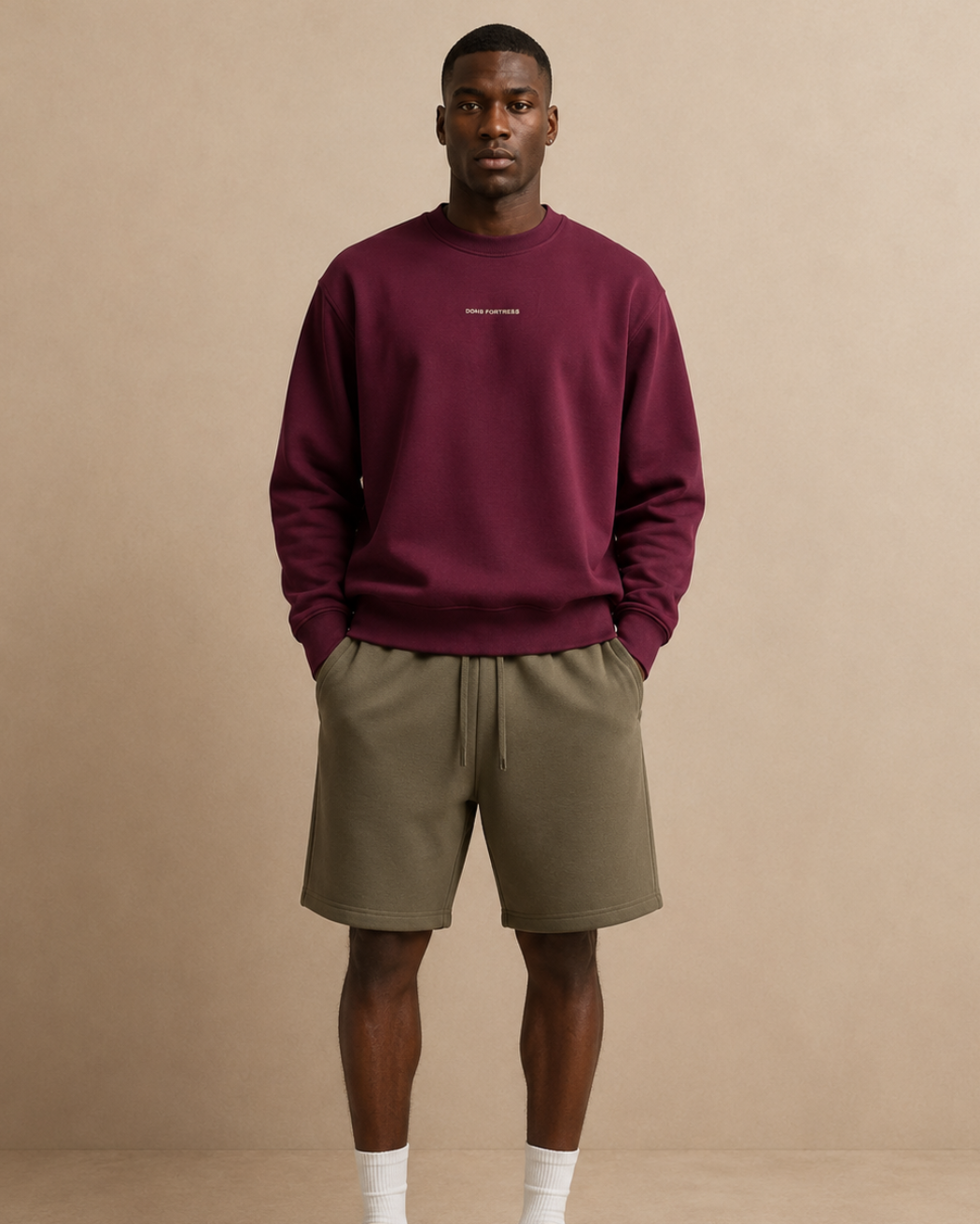 Man wearing a burgundy sweatshirt, beige shorts, and white sneakers against a beige background