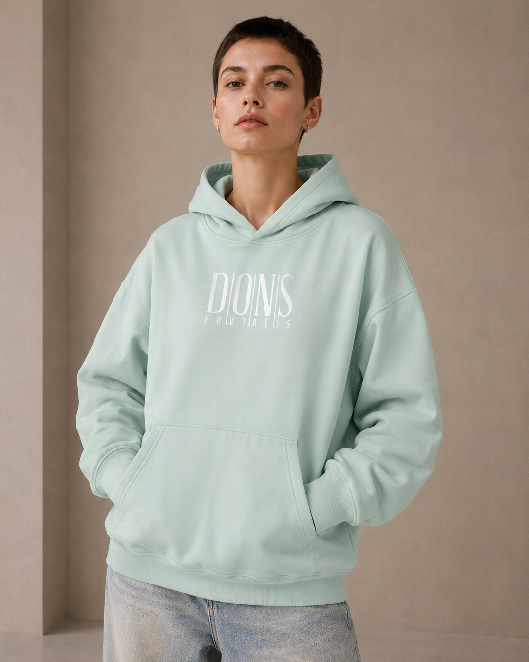 Person wearing a light green hoodie with branding on a beige background