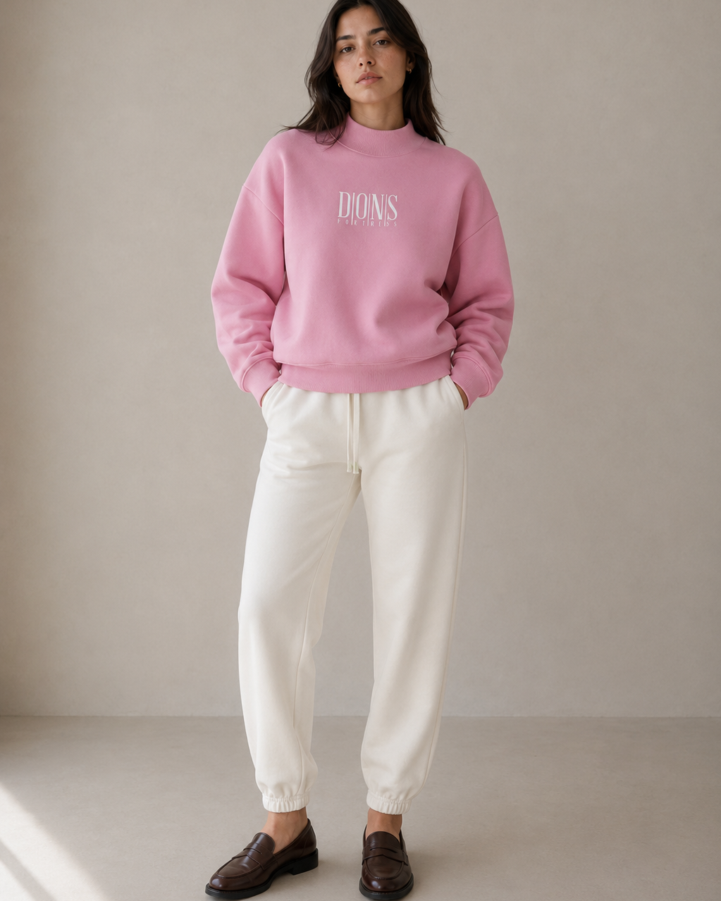 Person wearing a pink sweatshirt with text and white pants against a plain background