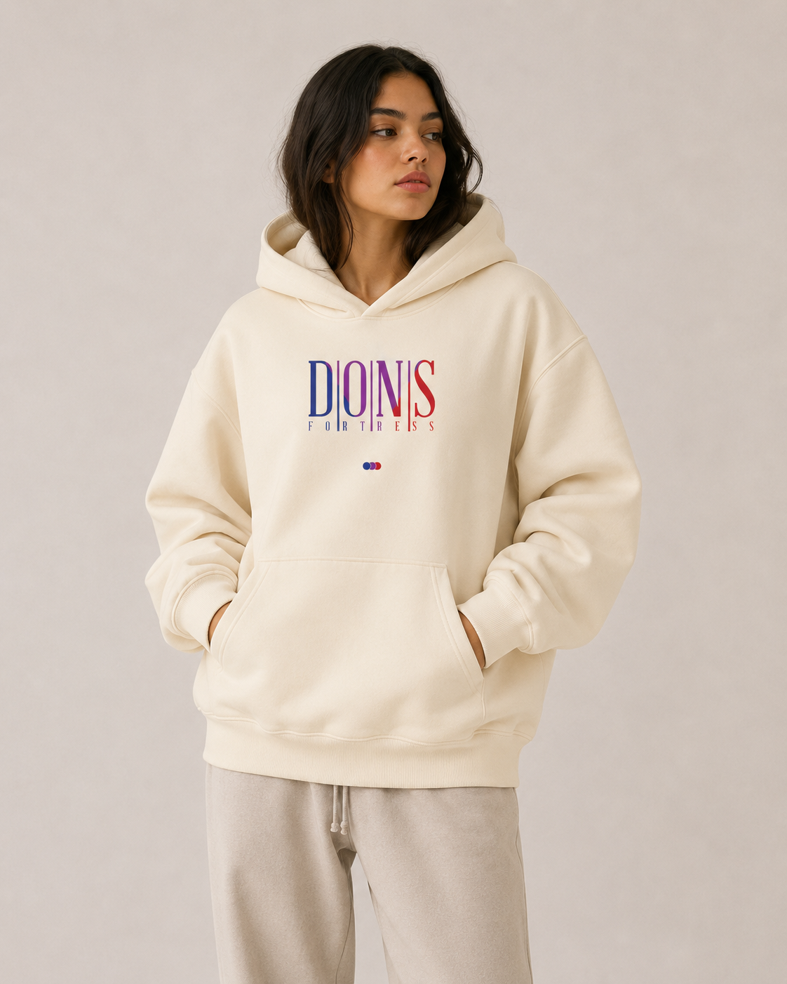 Person wearing a cream hoodie with branding on a plain background