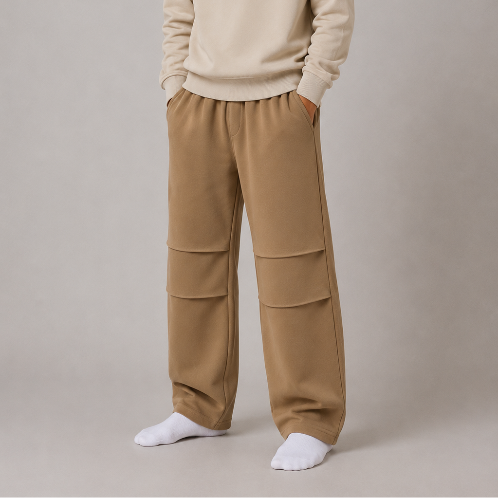 Person wearing a beige sweatshirt with colorful text and beige pants on a plain background