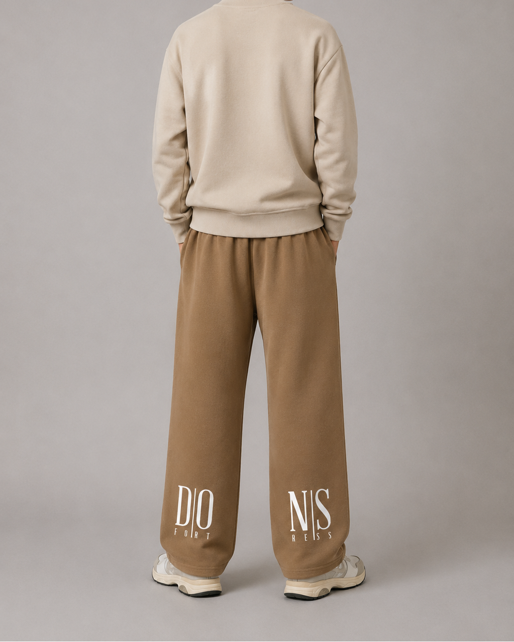 Person wearing a beige sweater and brown pants with visible branding on a gray background