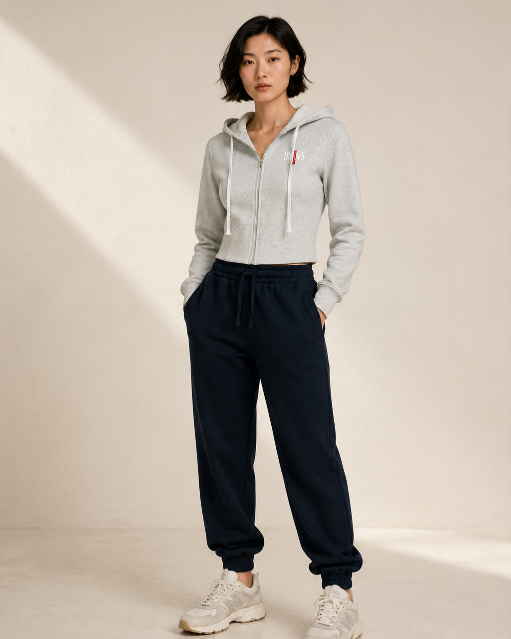 Person wearing a light gray hoodie and navy sweatpants on a neutral background
