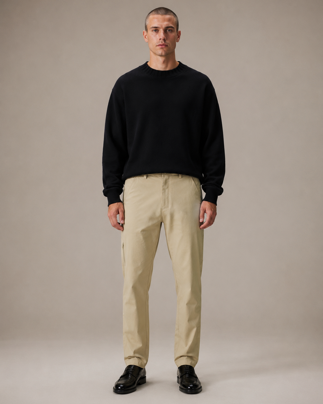 Man wearing a black sweater and beige pants against a neutral background