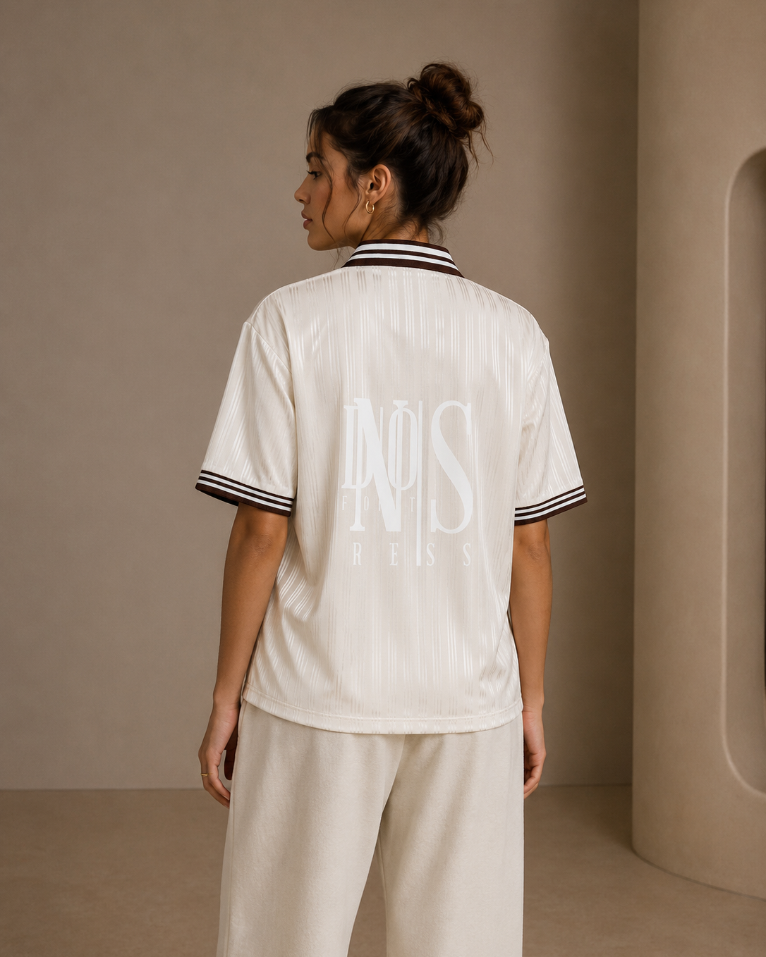 Person wearing a white shirt with text and beige pants in a minimalistic setting