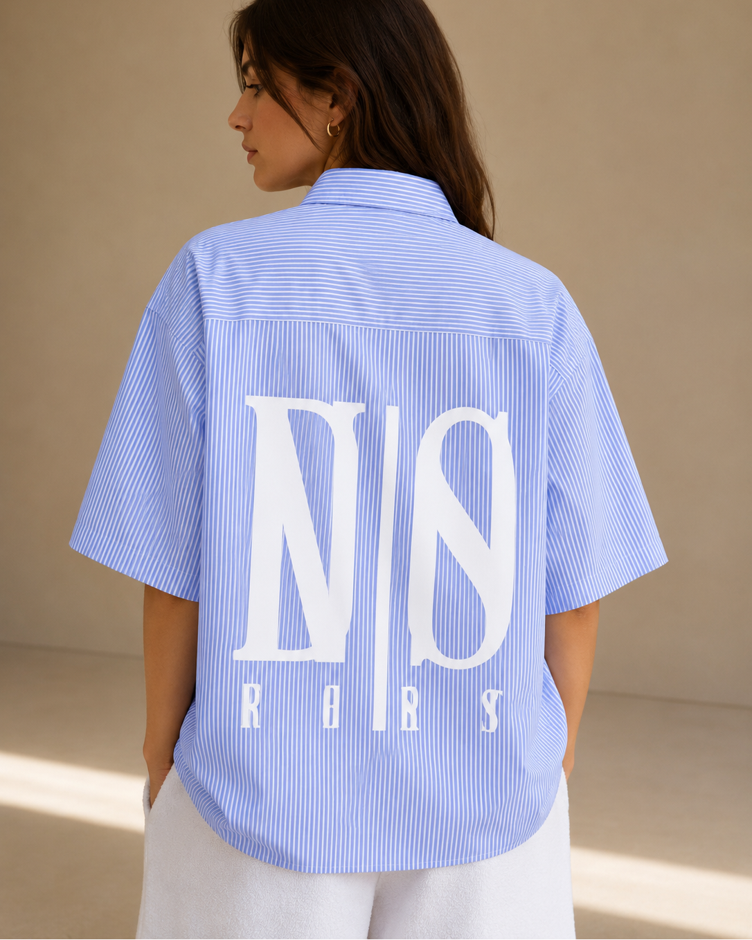 Woman wearing a blue striped shirt with a logo on the back against a beige background