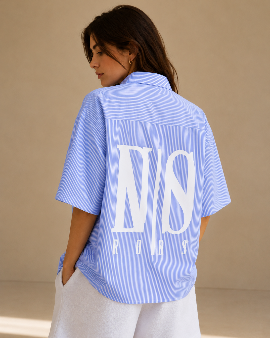 Woman wearing a light blue shirt with a logo on the back against a beige background