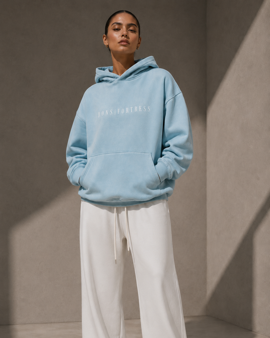 Person wearing a light blue hoodie and white pants against a neutral background
