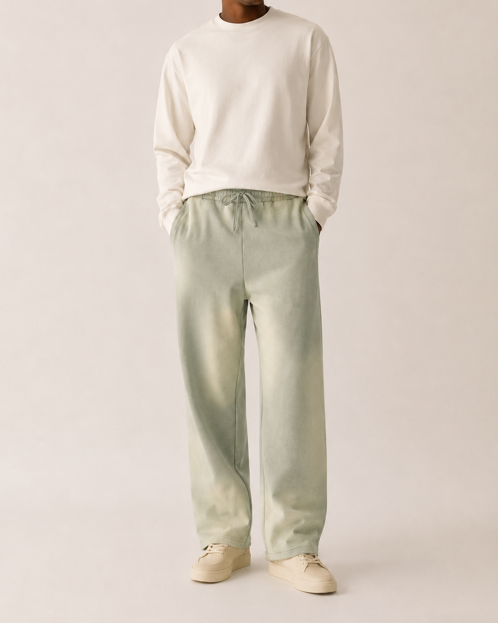 Man wearing a white sweater and light green pants on a plain background