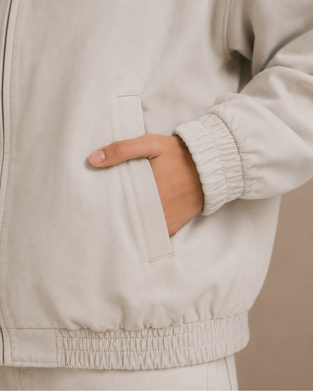 Close-up of a person wearing a beige jacket with a hand in the pocket against a neutral background