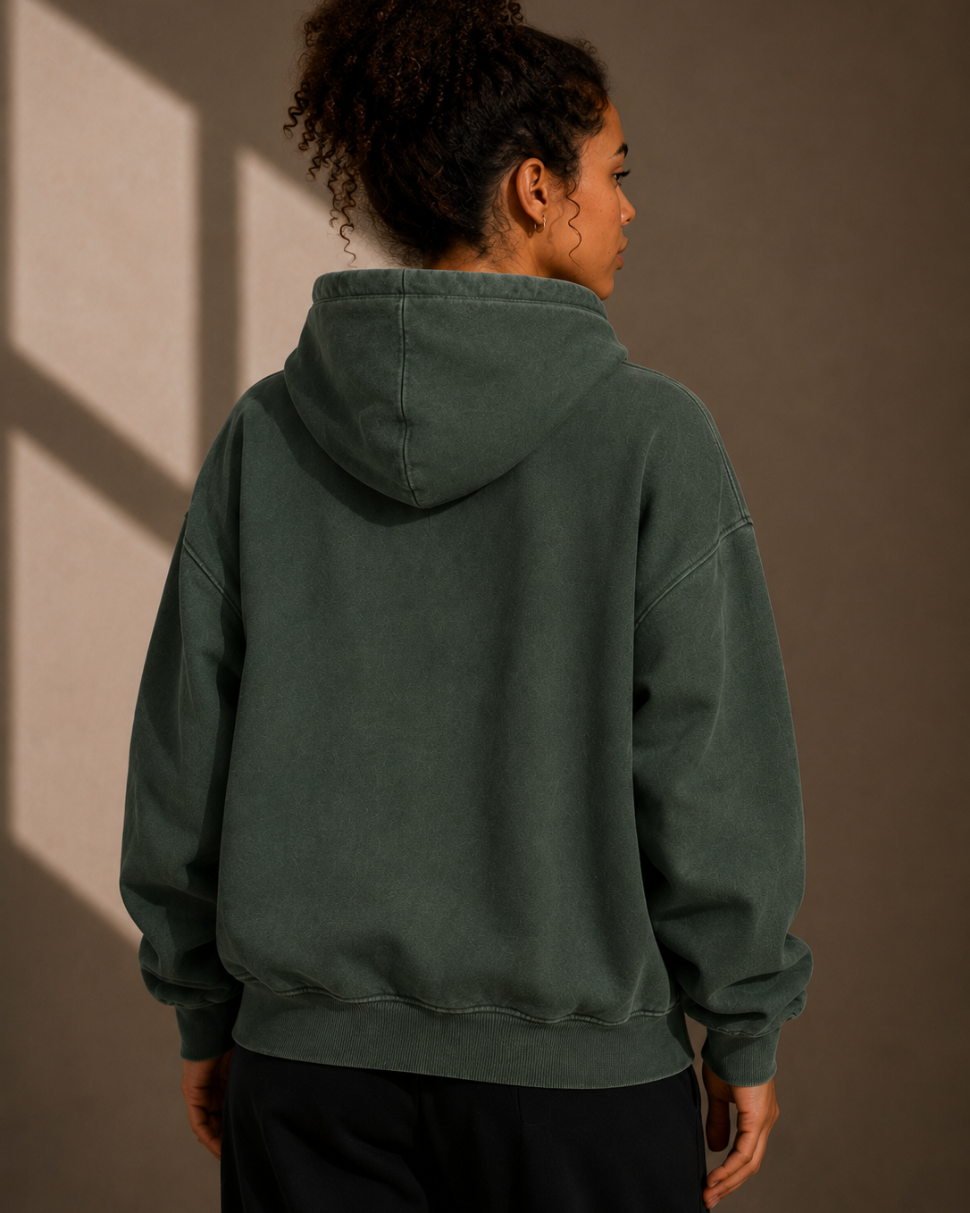 Person wearing a dark green hoodie against a brown background