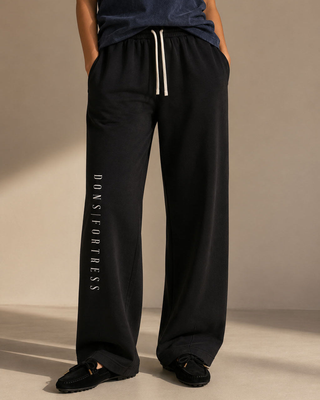 Person wearing black pants with 'Donsfortress' branding on a beige background