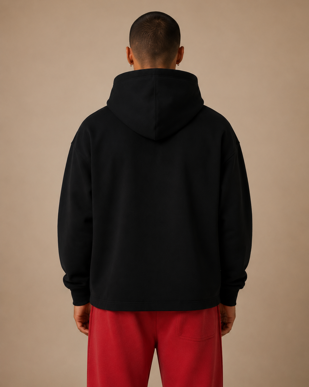 Person wearing a black hoodie and red pants against a beige background