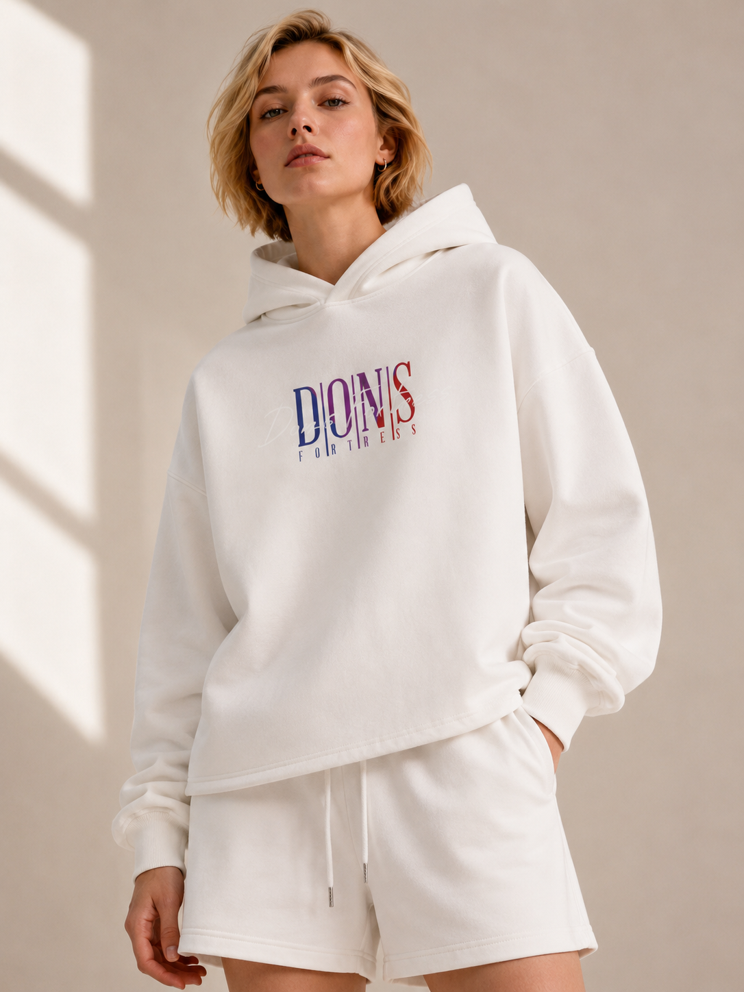 Person wearing a white hoodie with branding on a beige background