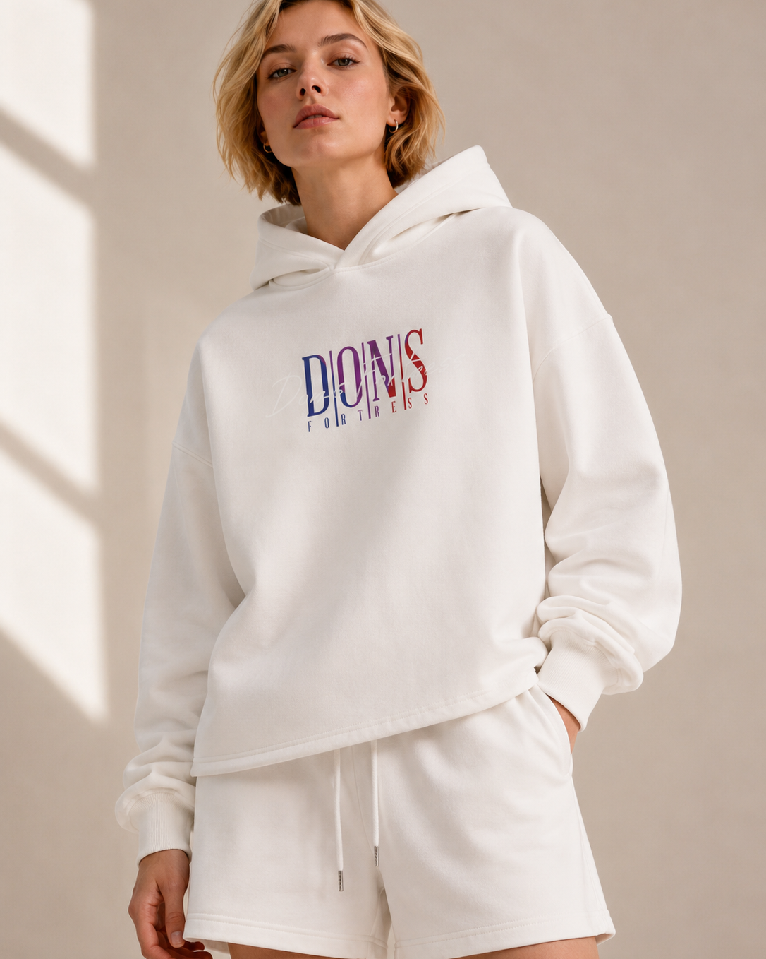 Person wearing a white hoodie with branding on a beige background