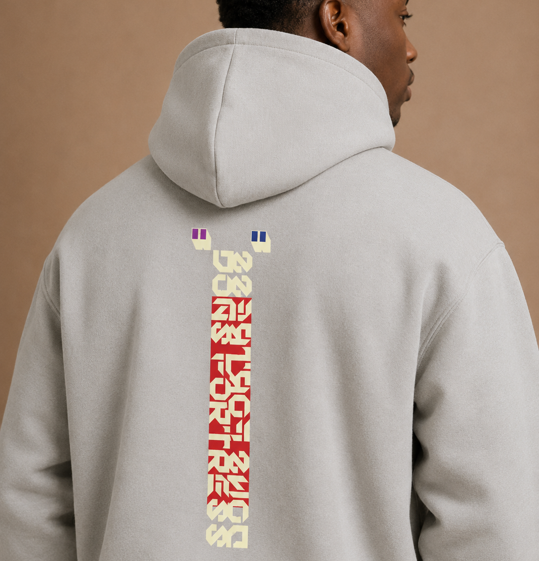 Person wearing a light gray hoodie with colorful text on the back against a beige background