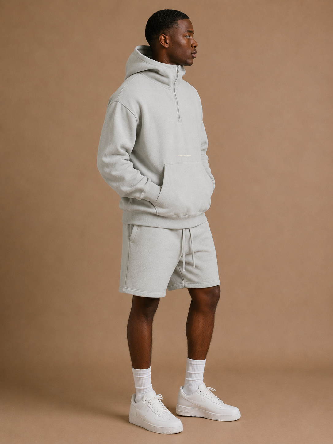 Man wearing a light gray hoodie and shorts set on a brown background