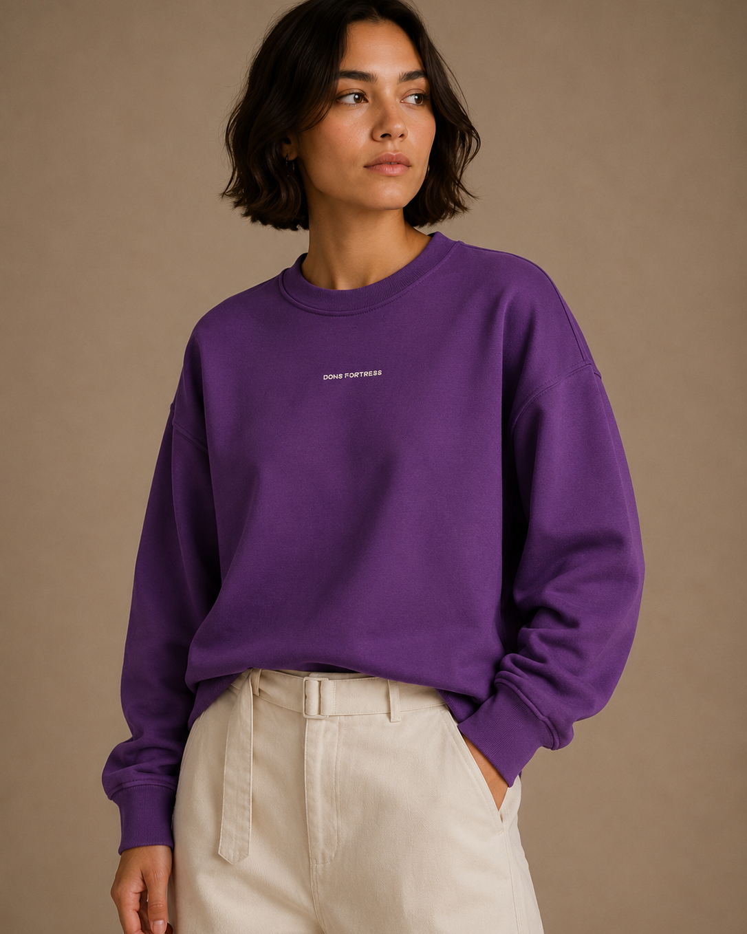 Person wearing a purple sweatshirt with a logo on a beige background