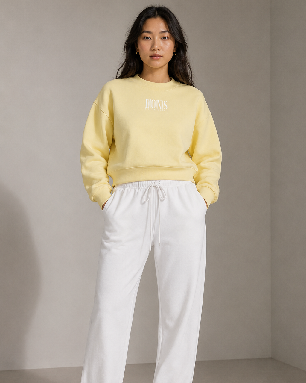 Person wearing a yellow sweatshirt and white pants against a neutral background
