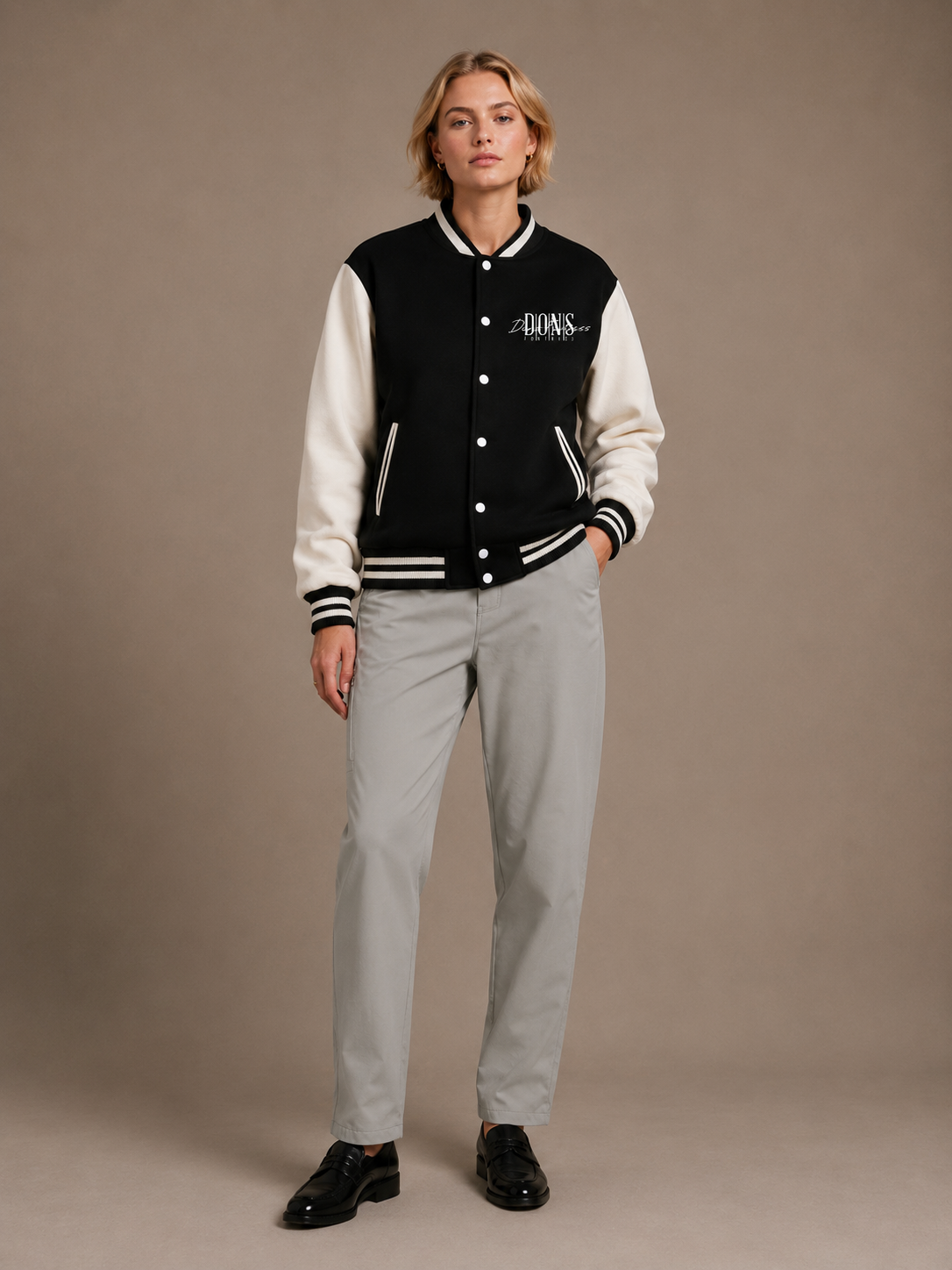 Person wearing a black and white varsity jacket with a logo, standing against a plain background