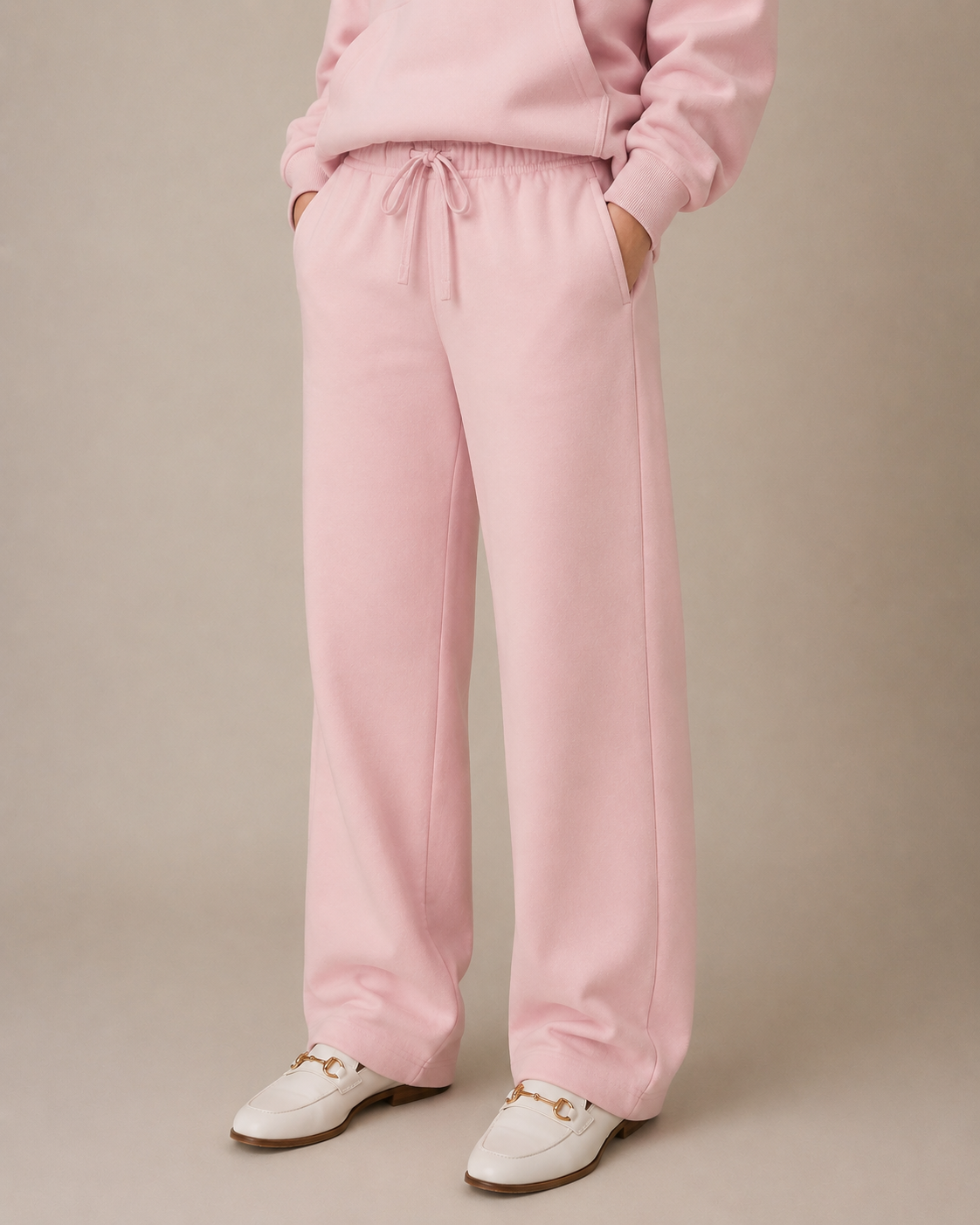 Person wearing a pink tracksuit with white shoes on a beige background