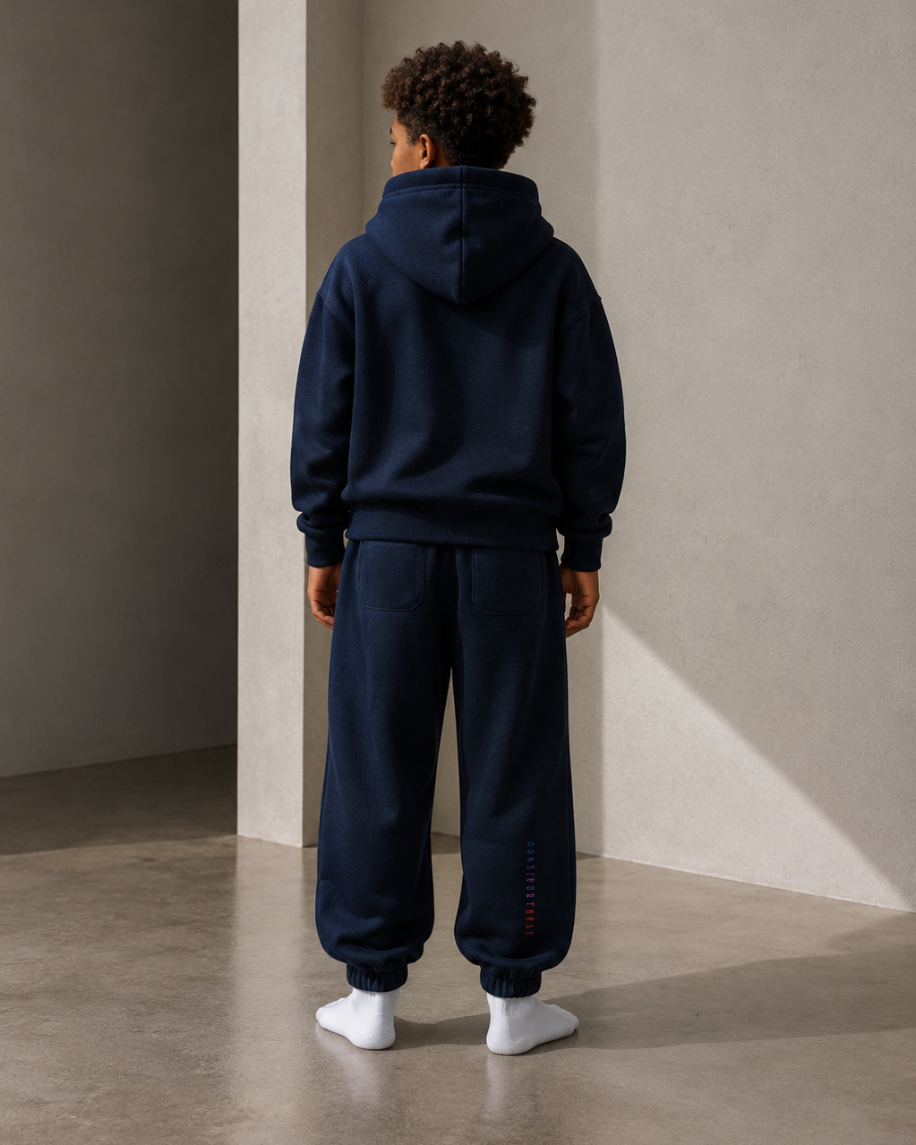 Person wearing a navy tracksuit standing against a plain wall.
