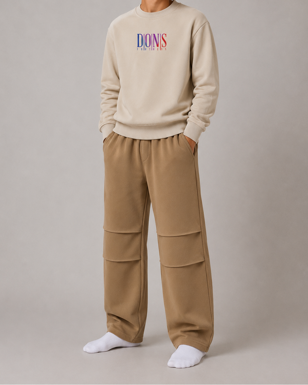Person wearing a beige sweatshirt with colorful text and beige pants on a plain background