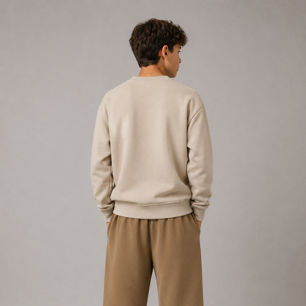 Person wearing a beige sweater and brown pants with visible branding on a gray background