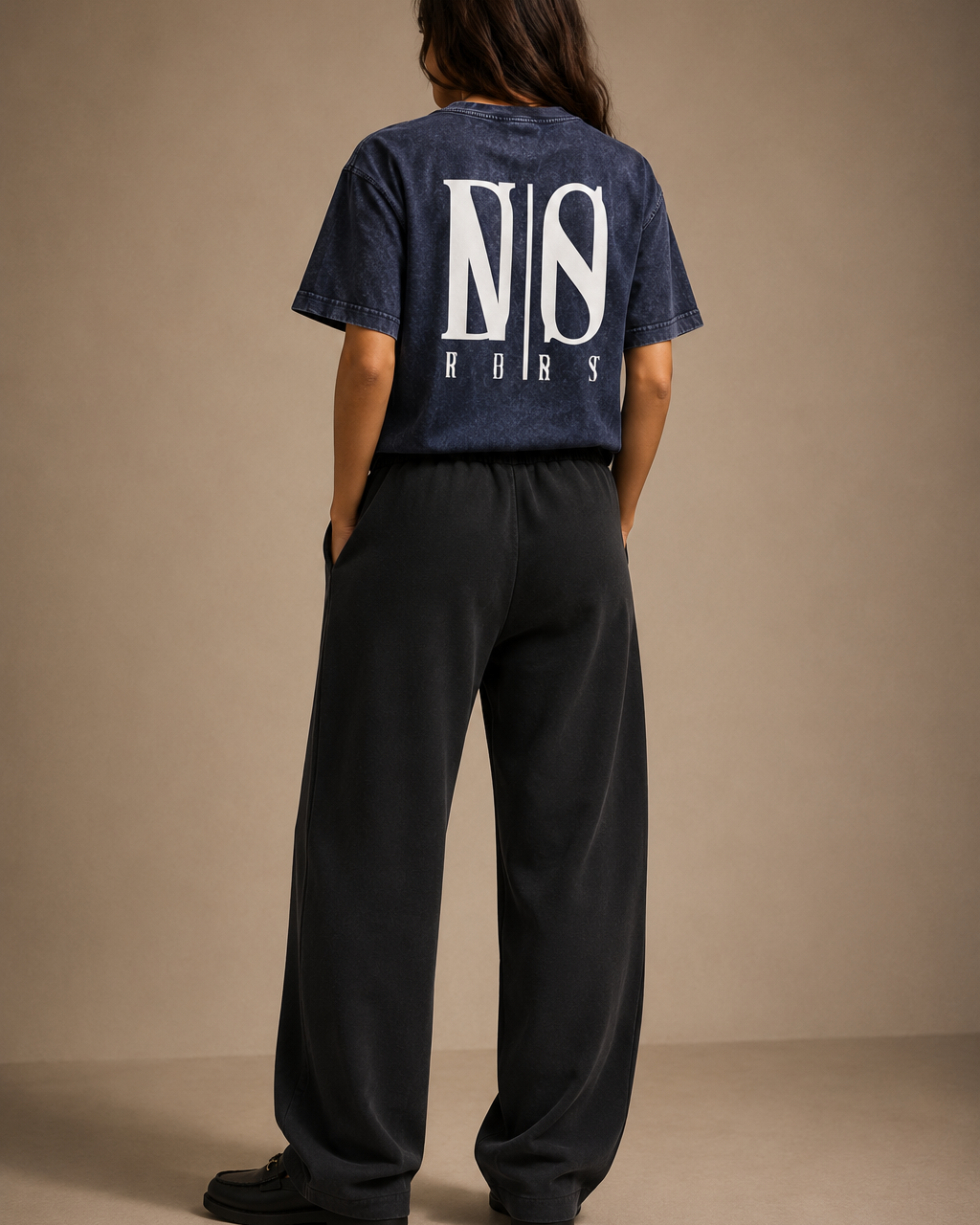 Person wearing a navy t-shirt with a logo on the back against a beige background
