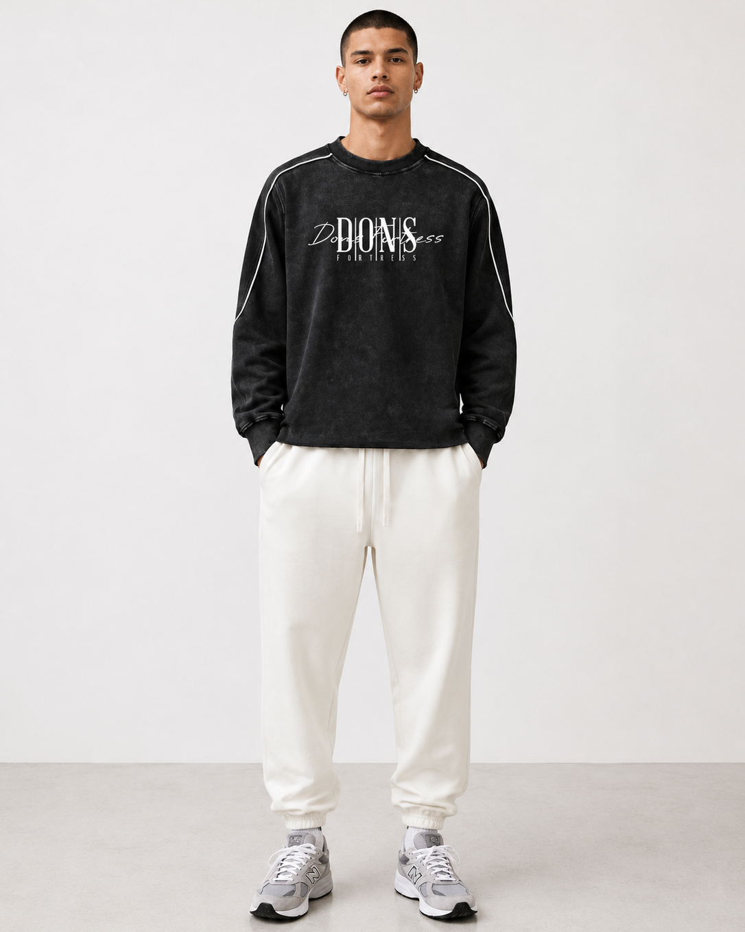Man wearing a black sweatshirt with white text and white pants on a white background
