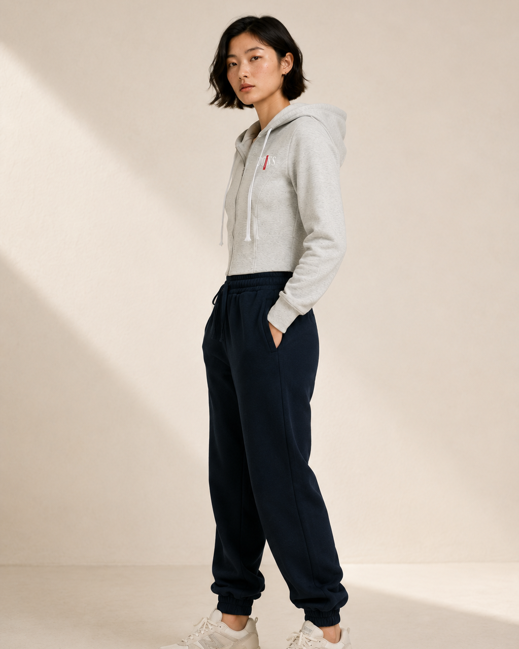 Person wearing a light gray hoodie and navy sweatpants on a beige background