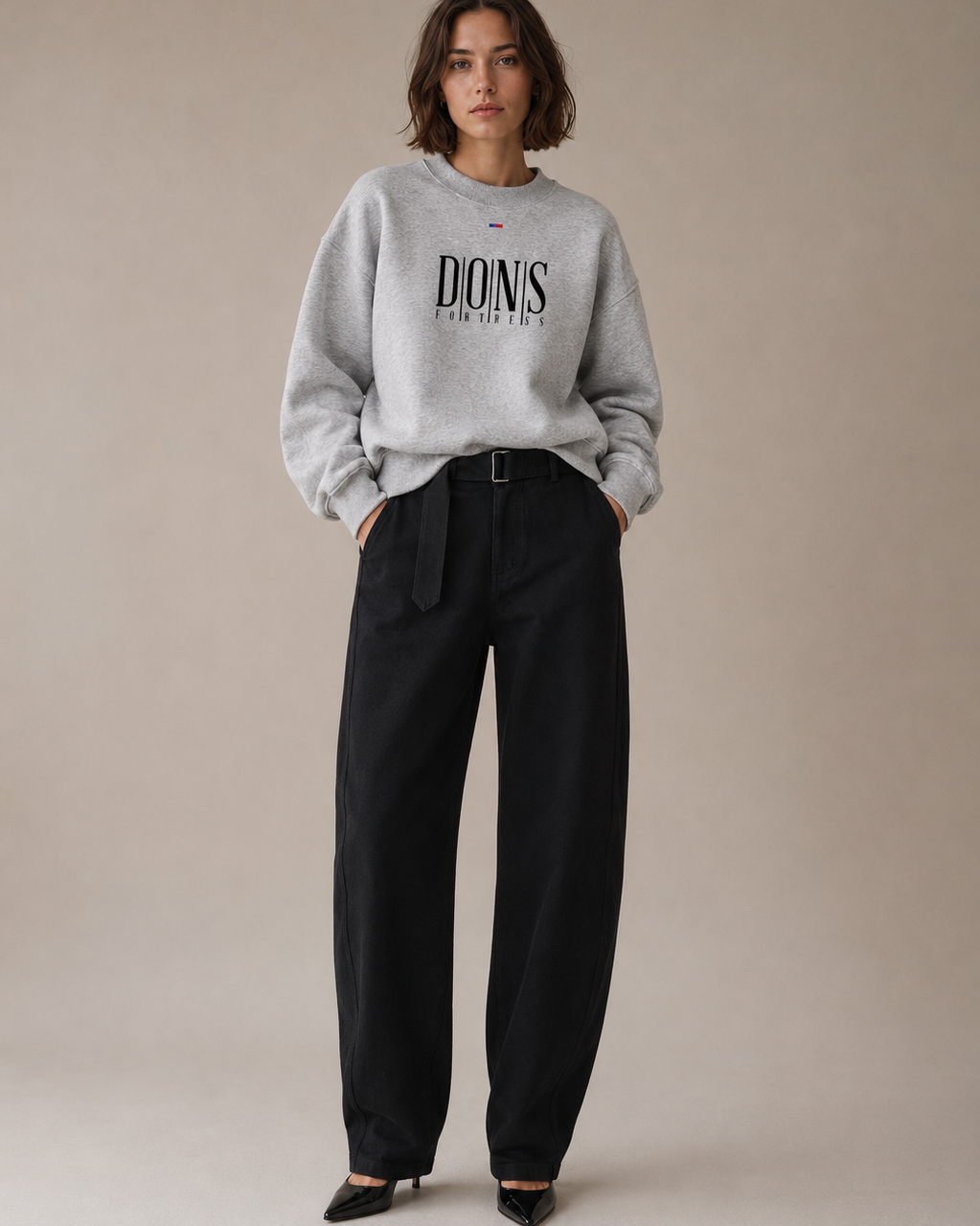 Woman wearing a gray sweatshirt with text and black pants on a beige background