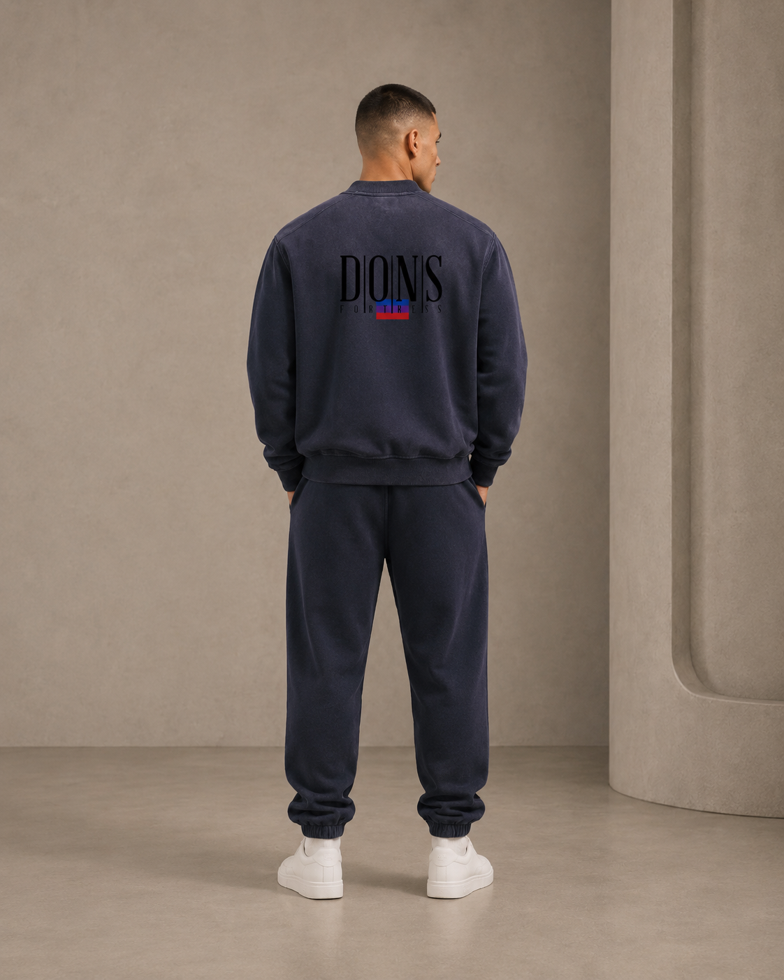 Person wearing a navy blue sweatshirt with branding on the back, standing against a beige wall.