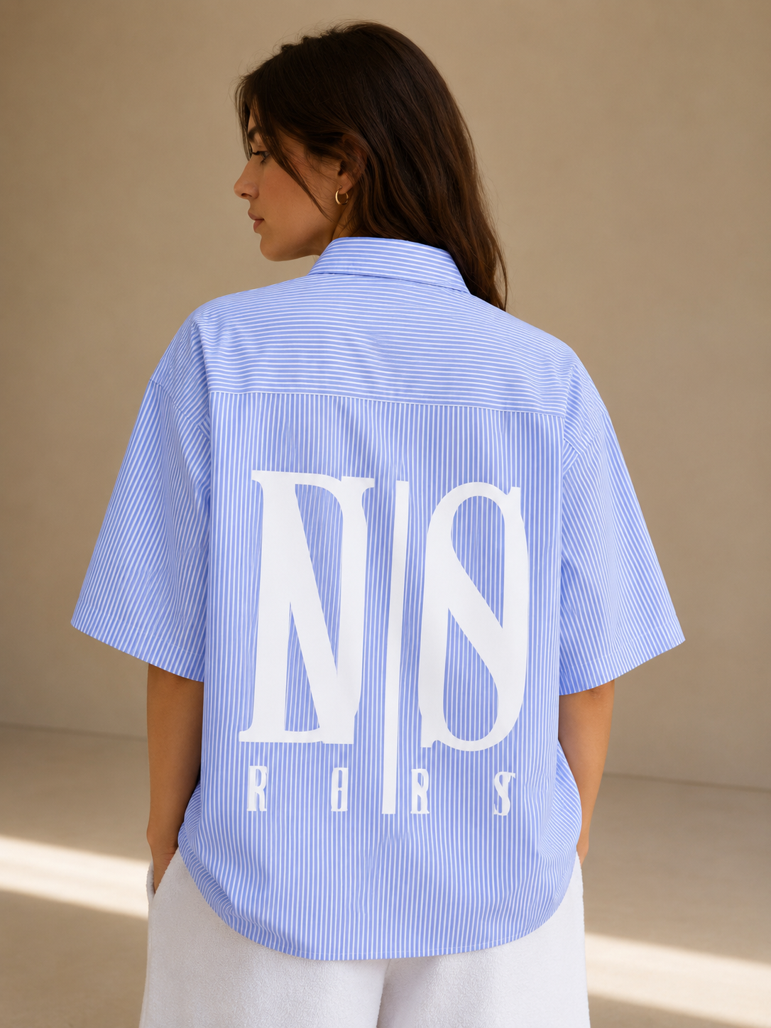 Woman wearing a blue striped shirt with a logo on the back against a beige background