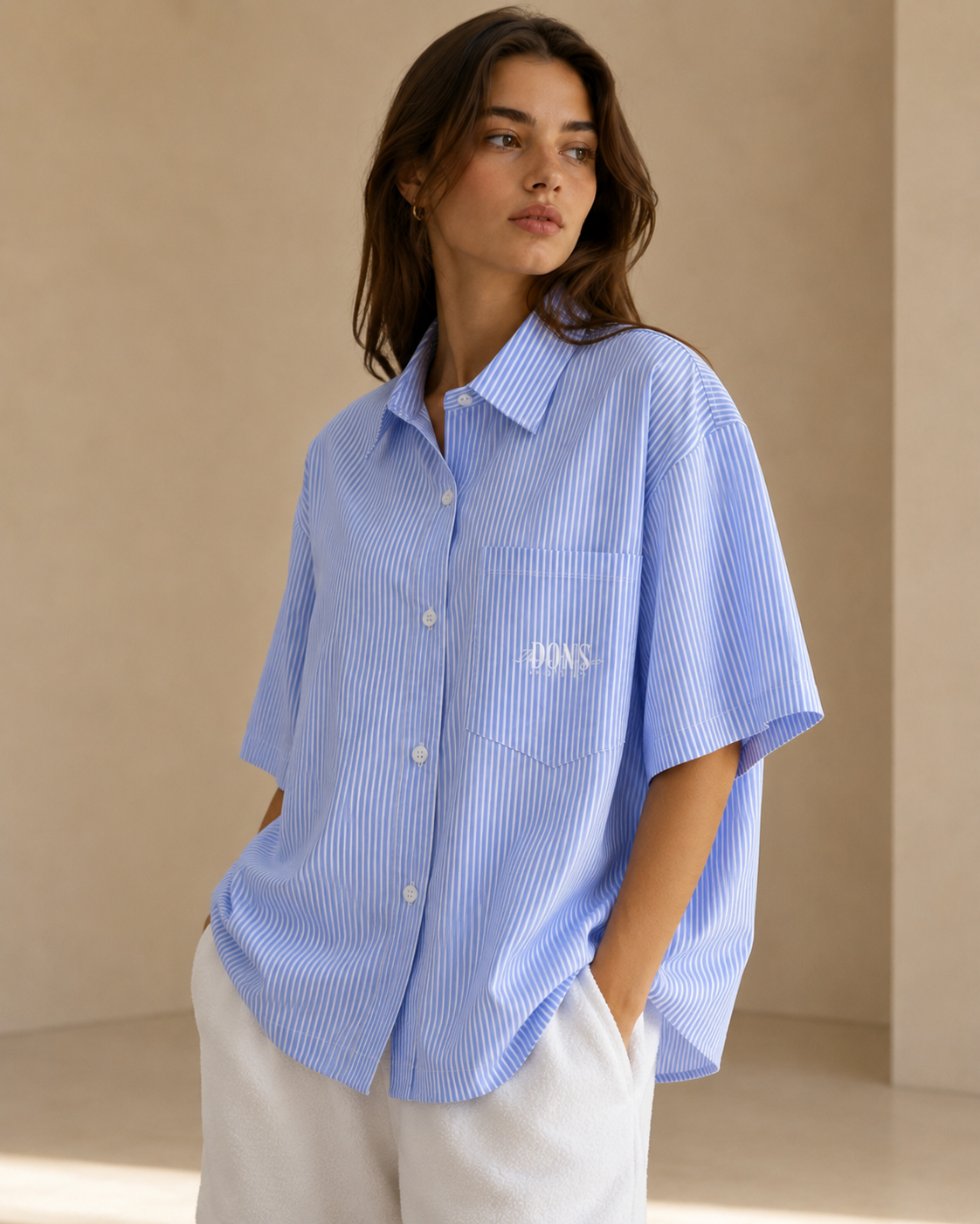 Woman wearing a blue striped shirt with a brand logo against a beige background