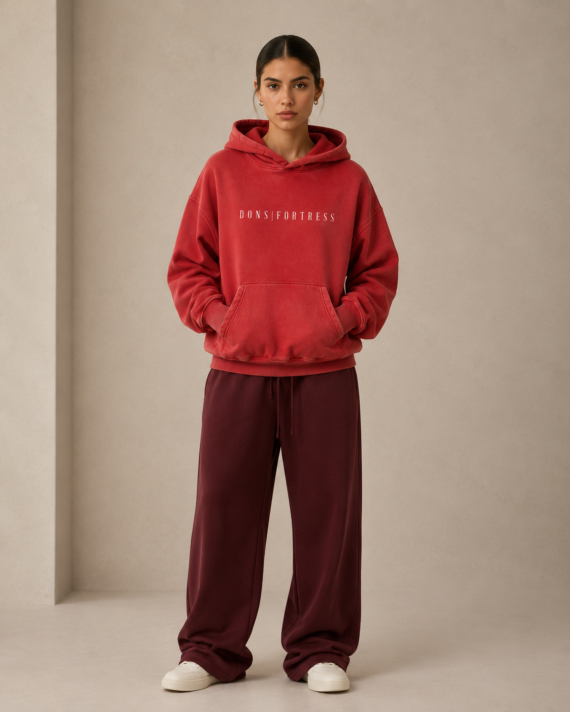 Person wearing a red hoodie and burgundy pants with 'DONS FORTRESS' branding on a beige background