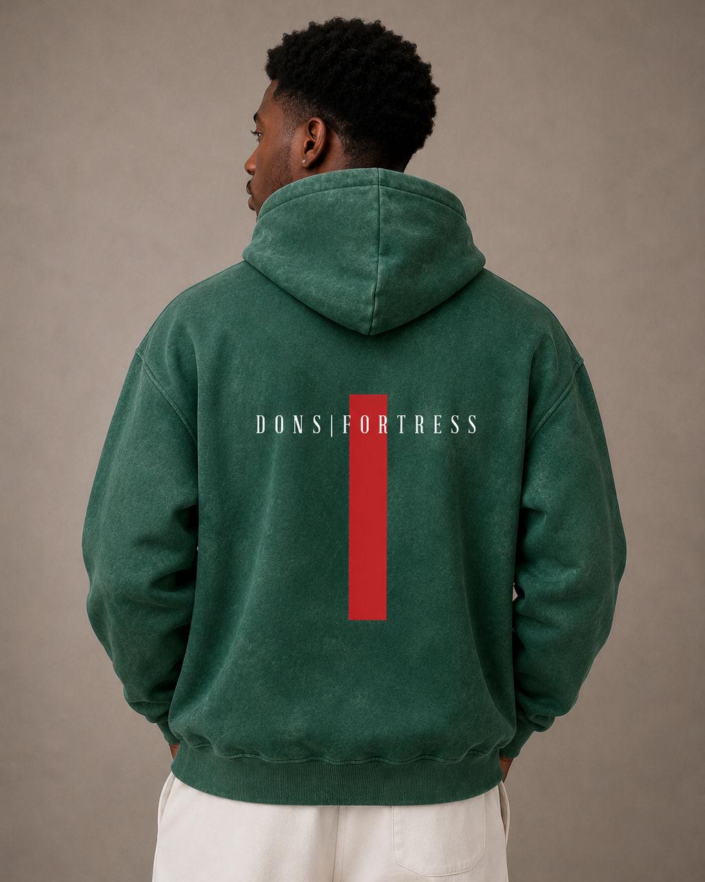 Person wearing a green hoodie with 'Dons fortress' logo on the back against a beige background