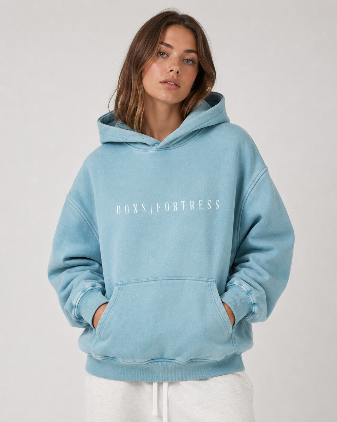 Person wearing a light blue hoodie with 'Dons Fortress' text on a plain background
