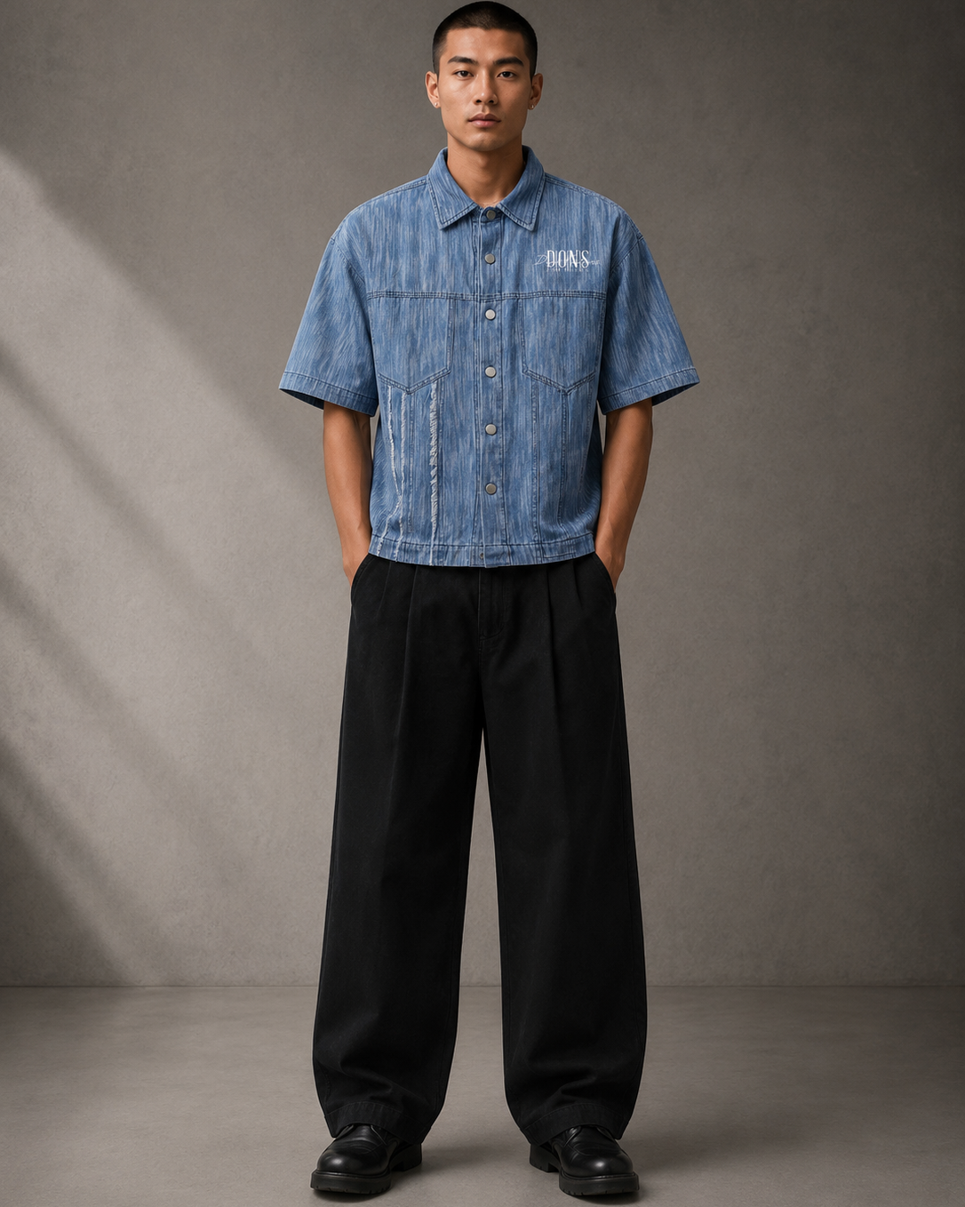 Man wearing a blue denim shirt and black pants against a gray background