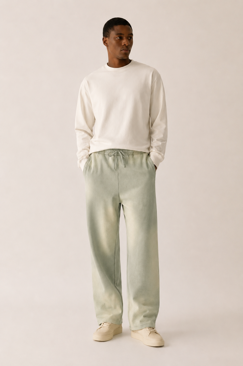 Man wearing a white sweater and light green pants on a plain background