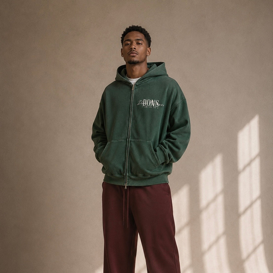 Man wearing a green hoodie with a logo on a beige wall