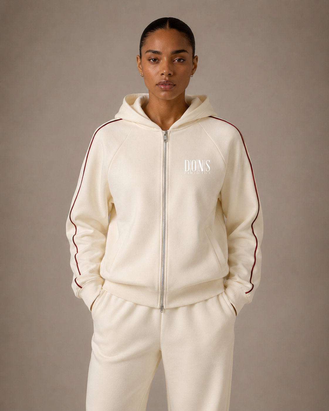 Person wearing a cream tracksuit with a brand logo on a plain background