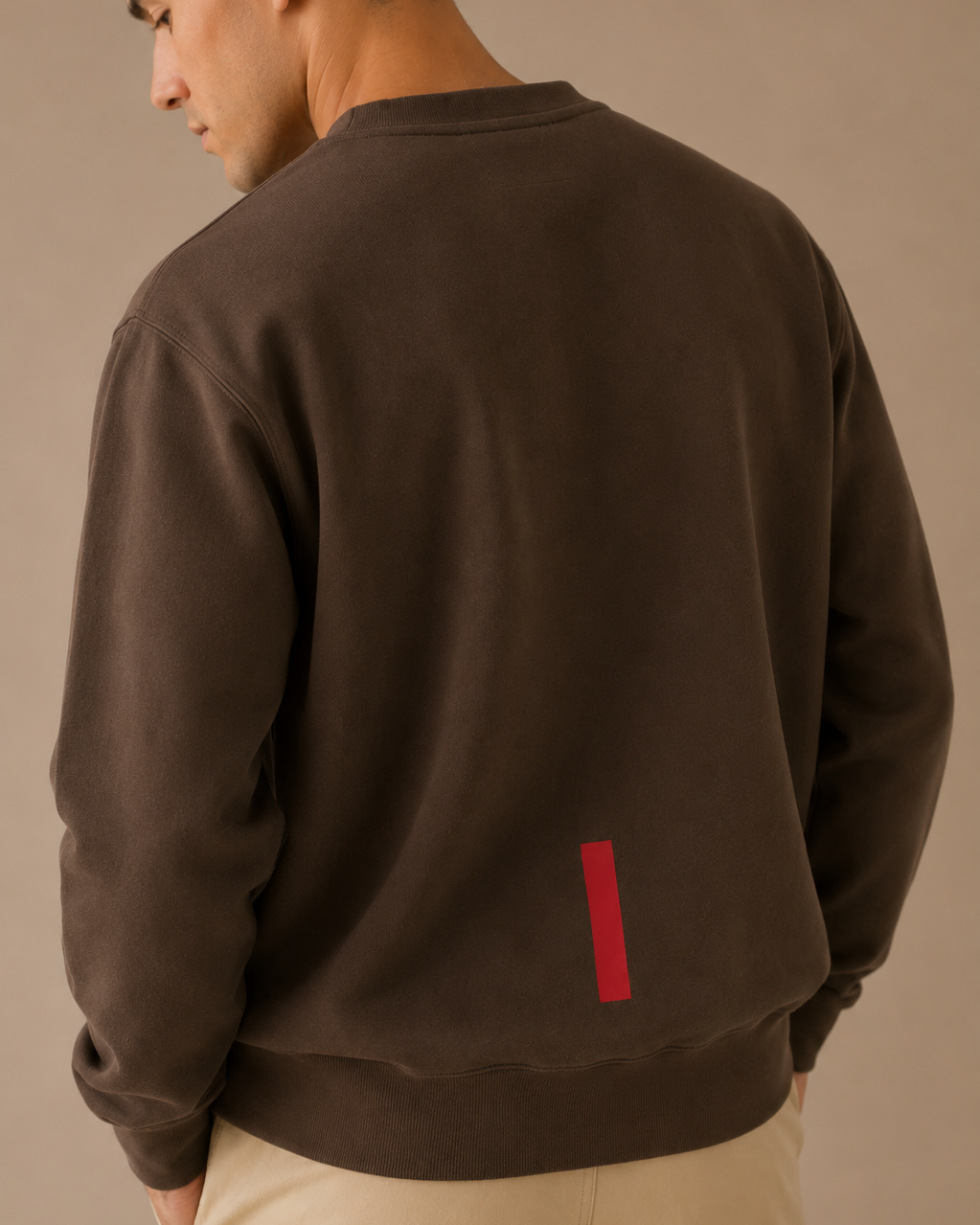 Man wearing a brown sweatshirt with a red rectangle on the back against a beige background